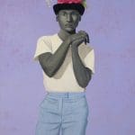 a painting by Amy sherald of a man wearing a top hat with flowers a white t-shirt and blue jeans holding his hands clasped together on his chest with a purple patterned background