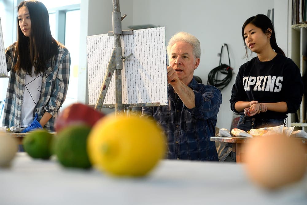 a man painting a still life image with a woman on his left looking over his shoulder, and a woman on his right painting her own image