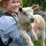 a girl with braided hair holding a small white lamb in her arms