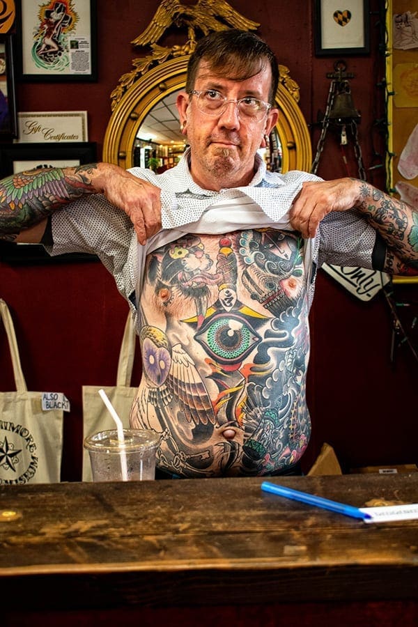 photo of man pulling up shirt to show tattooed stomach