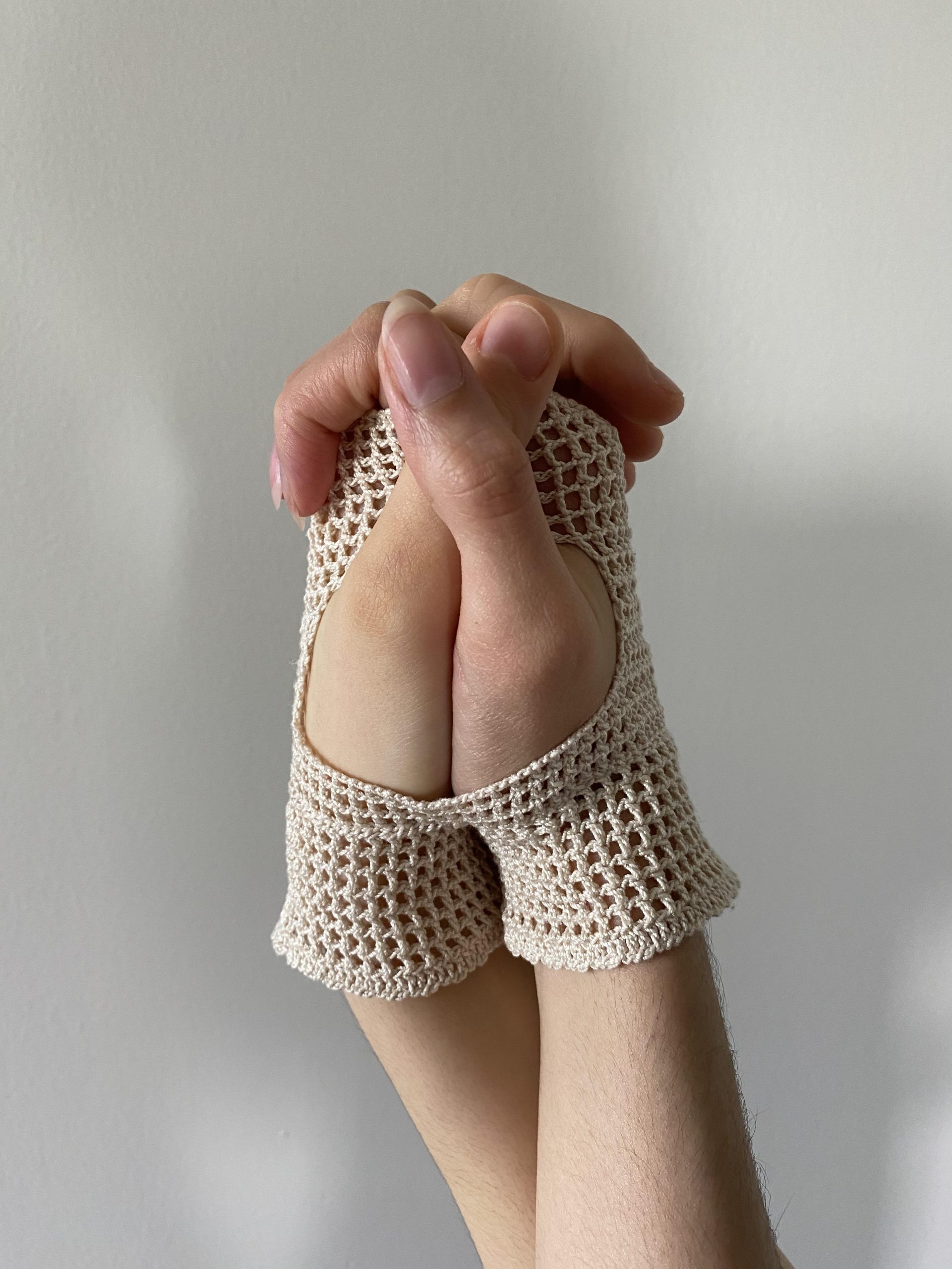 beige knitted hand covering with two hands clasped inside