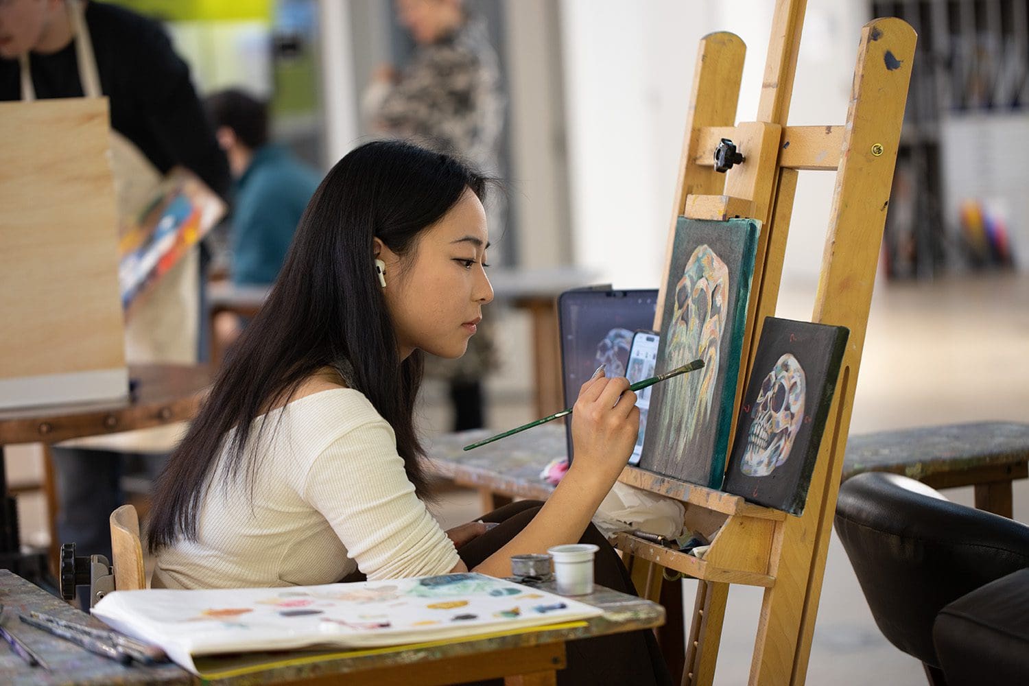 student at an easel, painting on a black piece of paper
