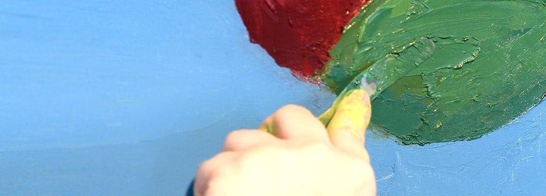 a close up of a hand using a palette knife to paint