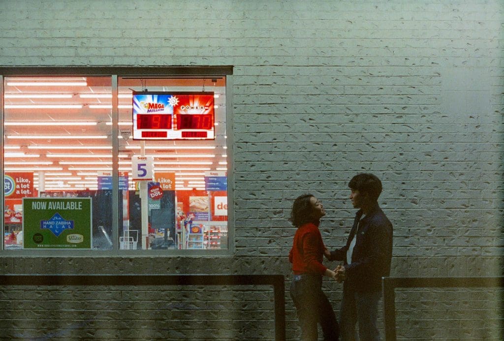 a girl and boy standing in front of a gas station wall with a window to their left