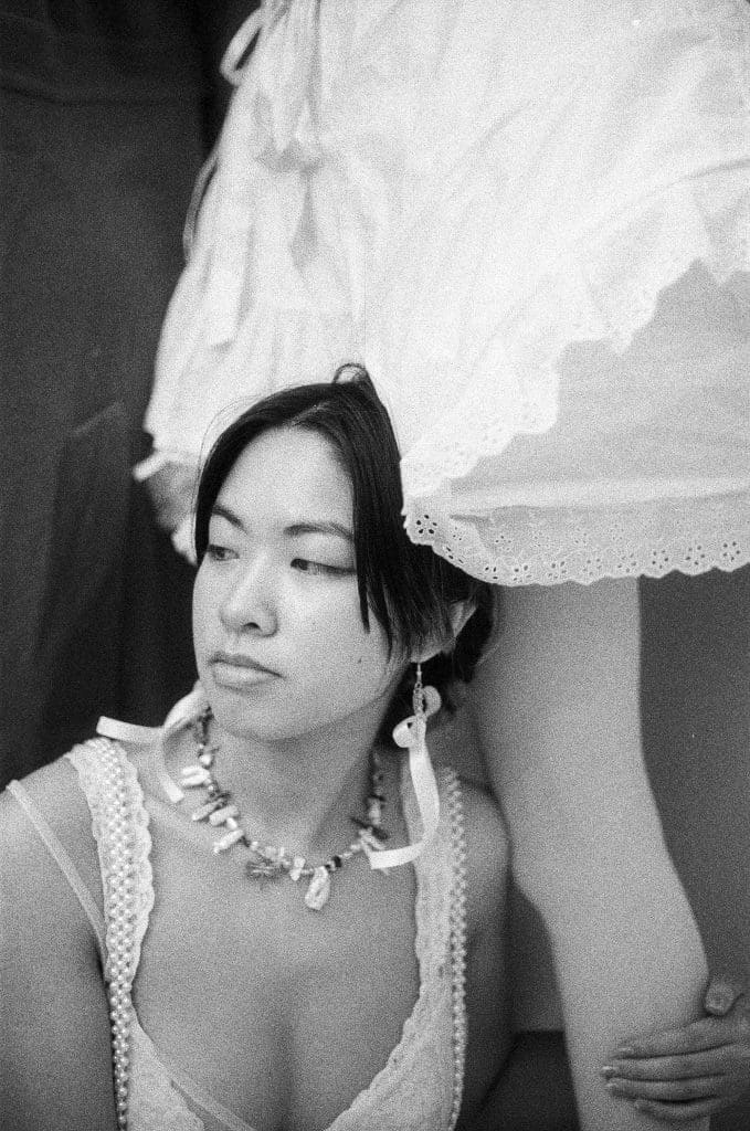 a girl sitting on the ground with her arm around the leg of a girl wearing a white dress