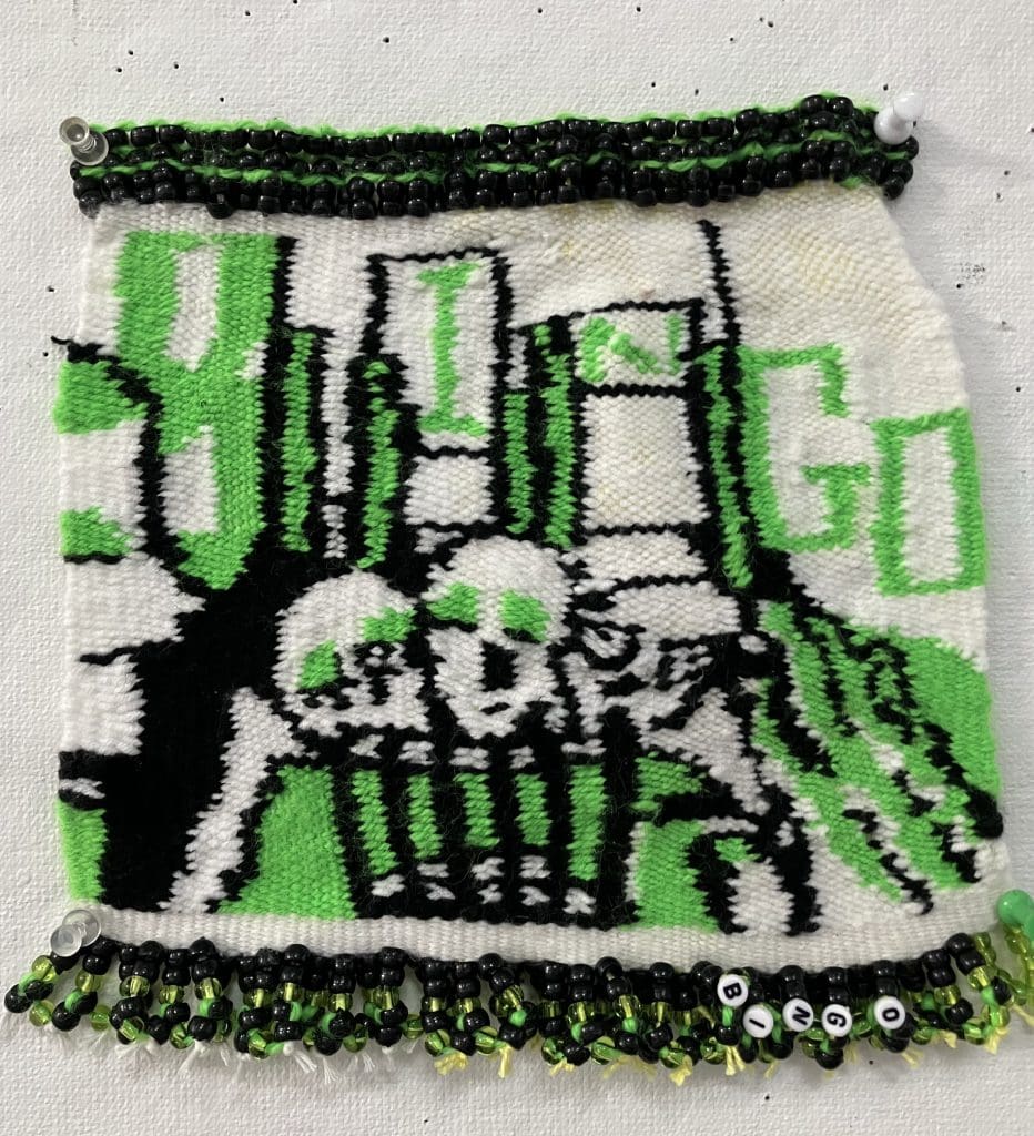 small weaved panel with image of two skulls and green and black designs that reads "bingo"