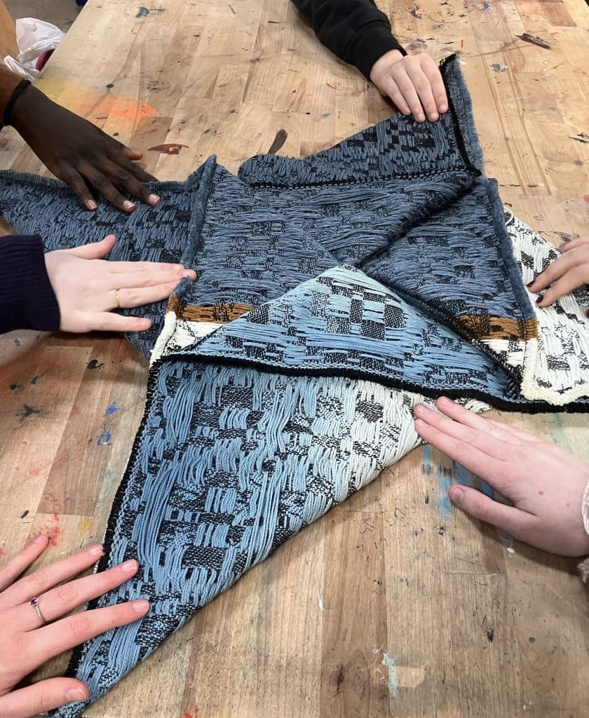 students touching a folded weaving