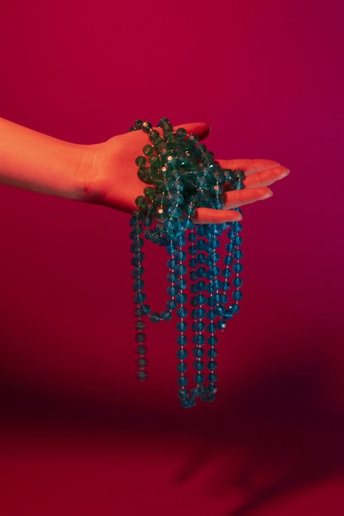 a hand holding a blue necklace in front of a red background