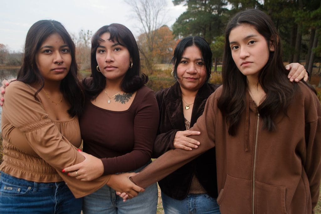 4 women of varying ages standing in a line facing the camera wearing brown