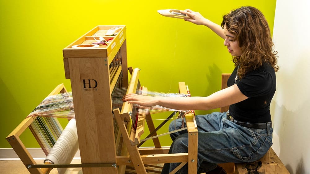 person using a knitting loom in front of a green wall