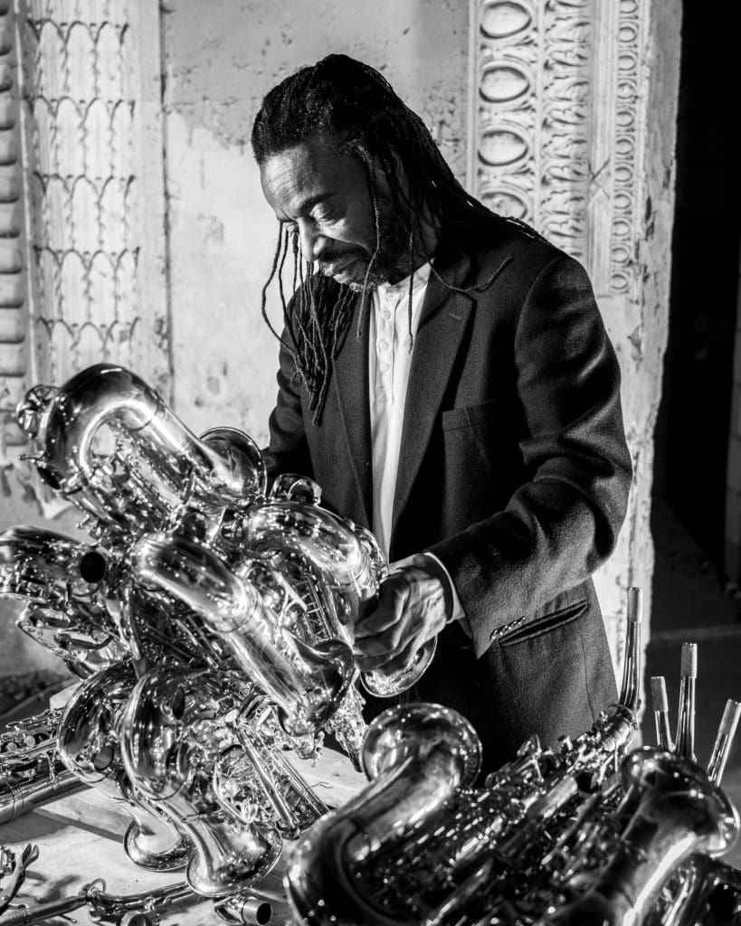 black and white image of artist Willie Cole standing with his saxophone bird sculpture