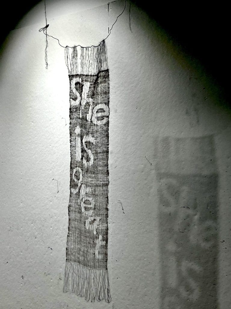 lace artwork hanging from ceiling with shadow that reads "she is great"