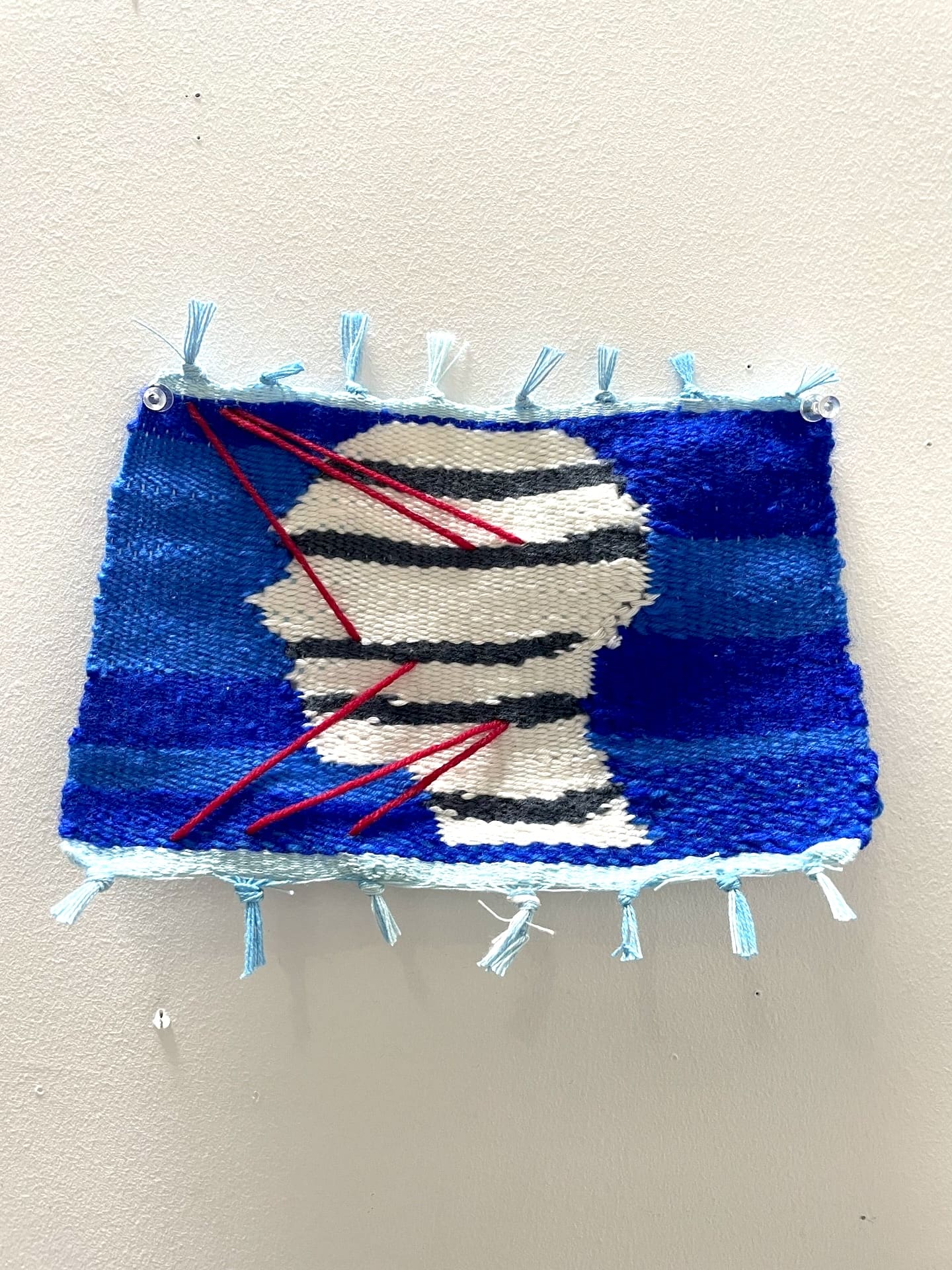 weaving of white silhouetted head with red and black stripes and blue background 