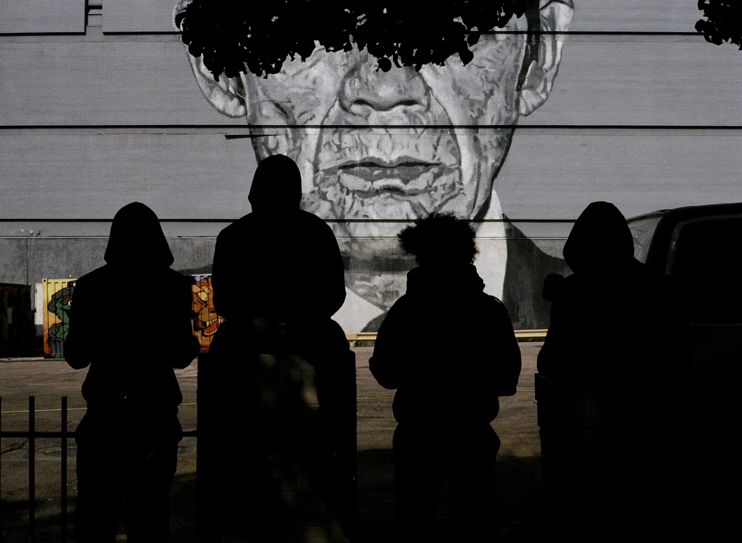 silhouettes of four people standing in front of a mural of a mans face