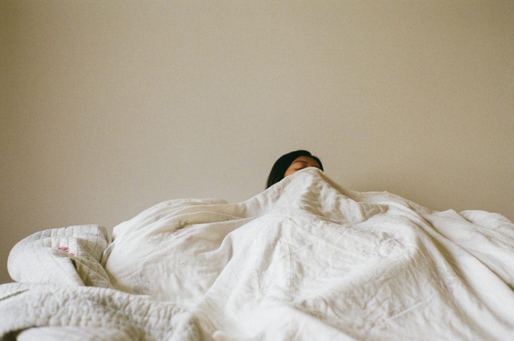 girl poking her face out from behind a comforter