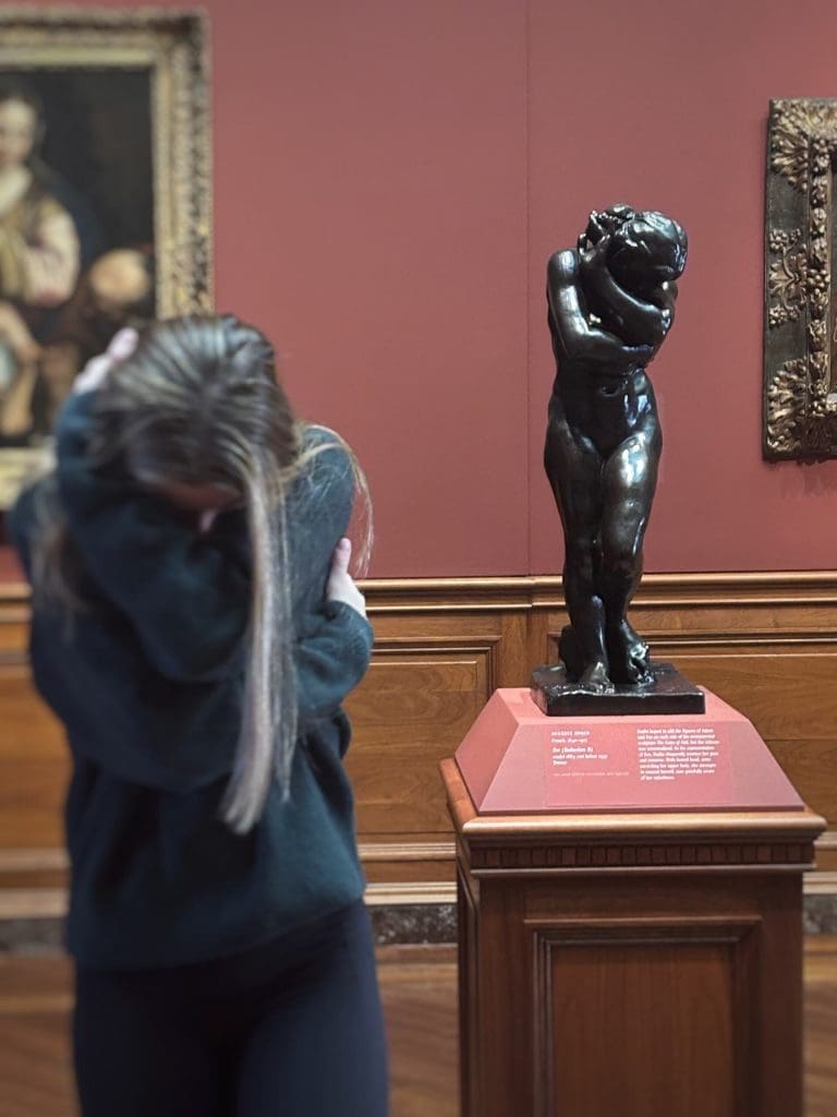 a girl copying the pose of a statue of a girl crossing her arms in front of her face