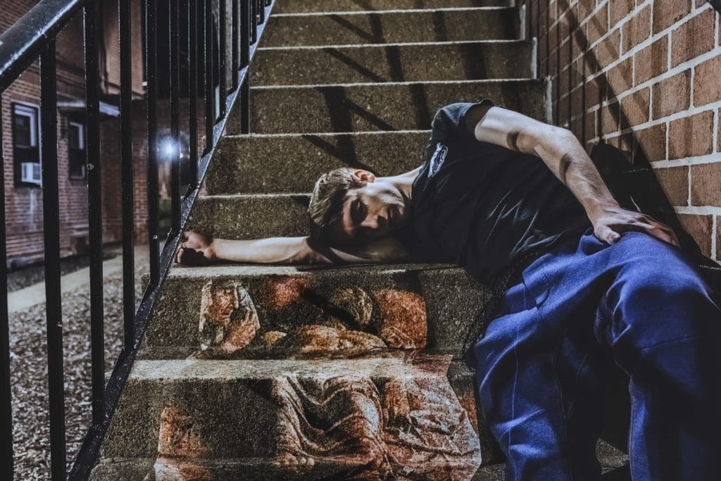 a man with short hair, a t shirt, and pmats laying eyes closed on a set of steps