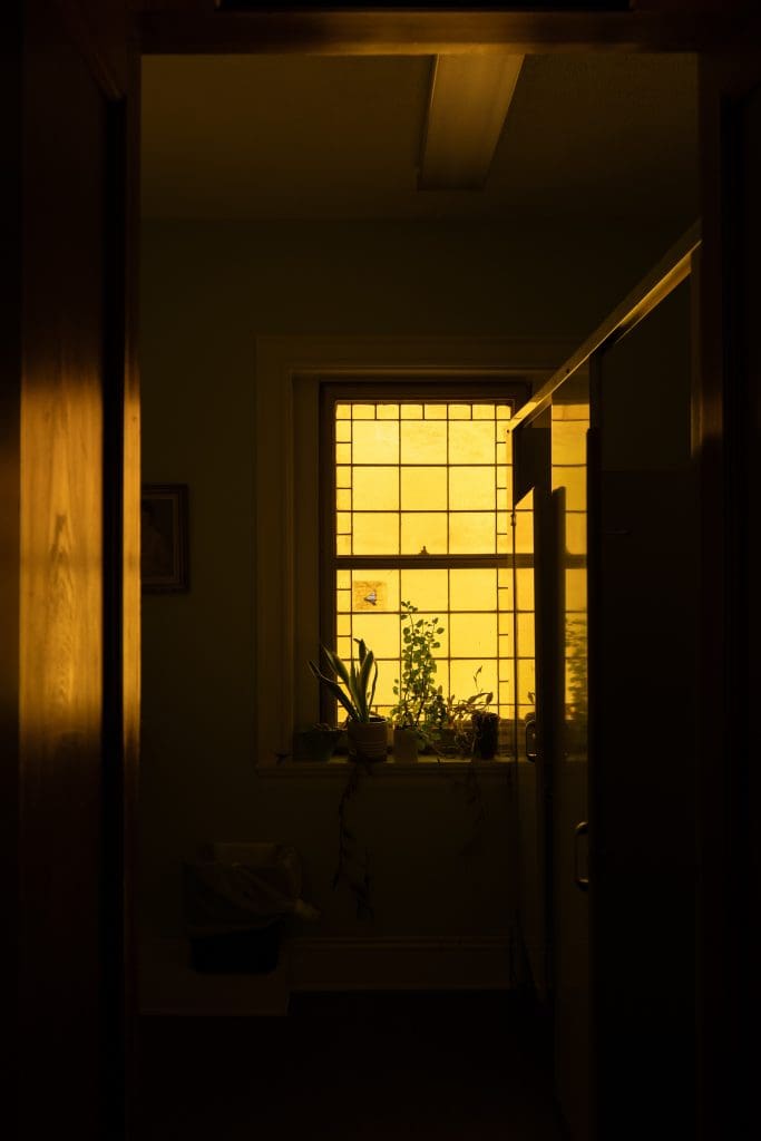 a yellow stained glass window in a dark lit bathroom