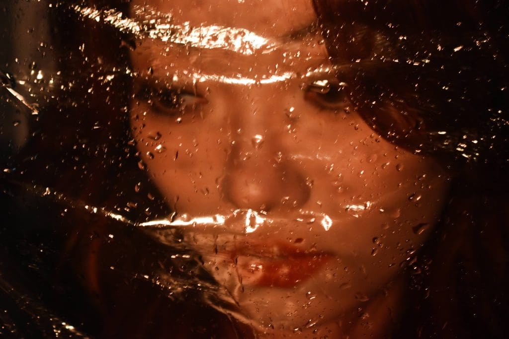 Girl with brown hair with water droplits on plastic film in front of her face