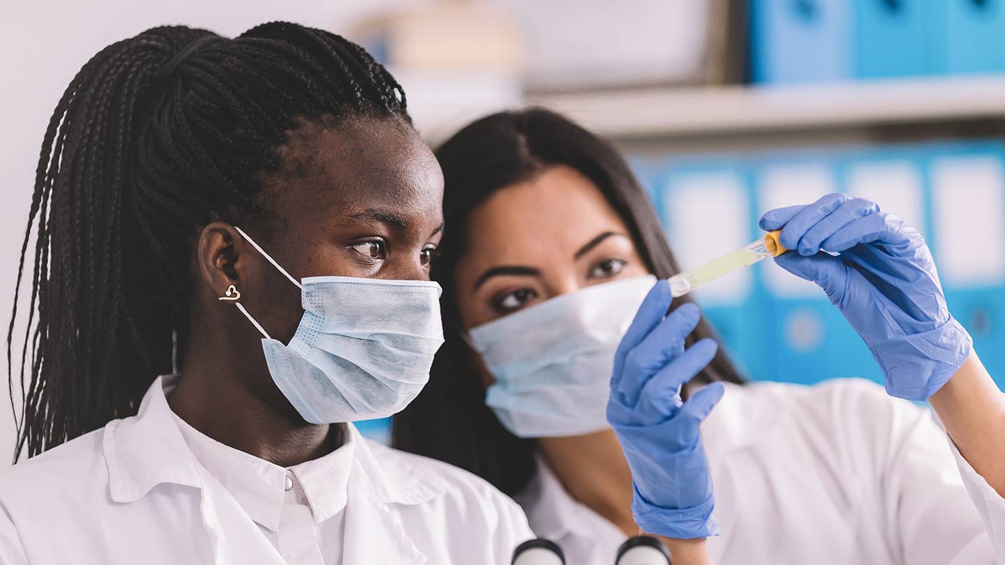 two women of color looking at a test tube while masked