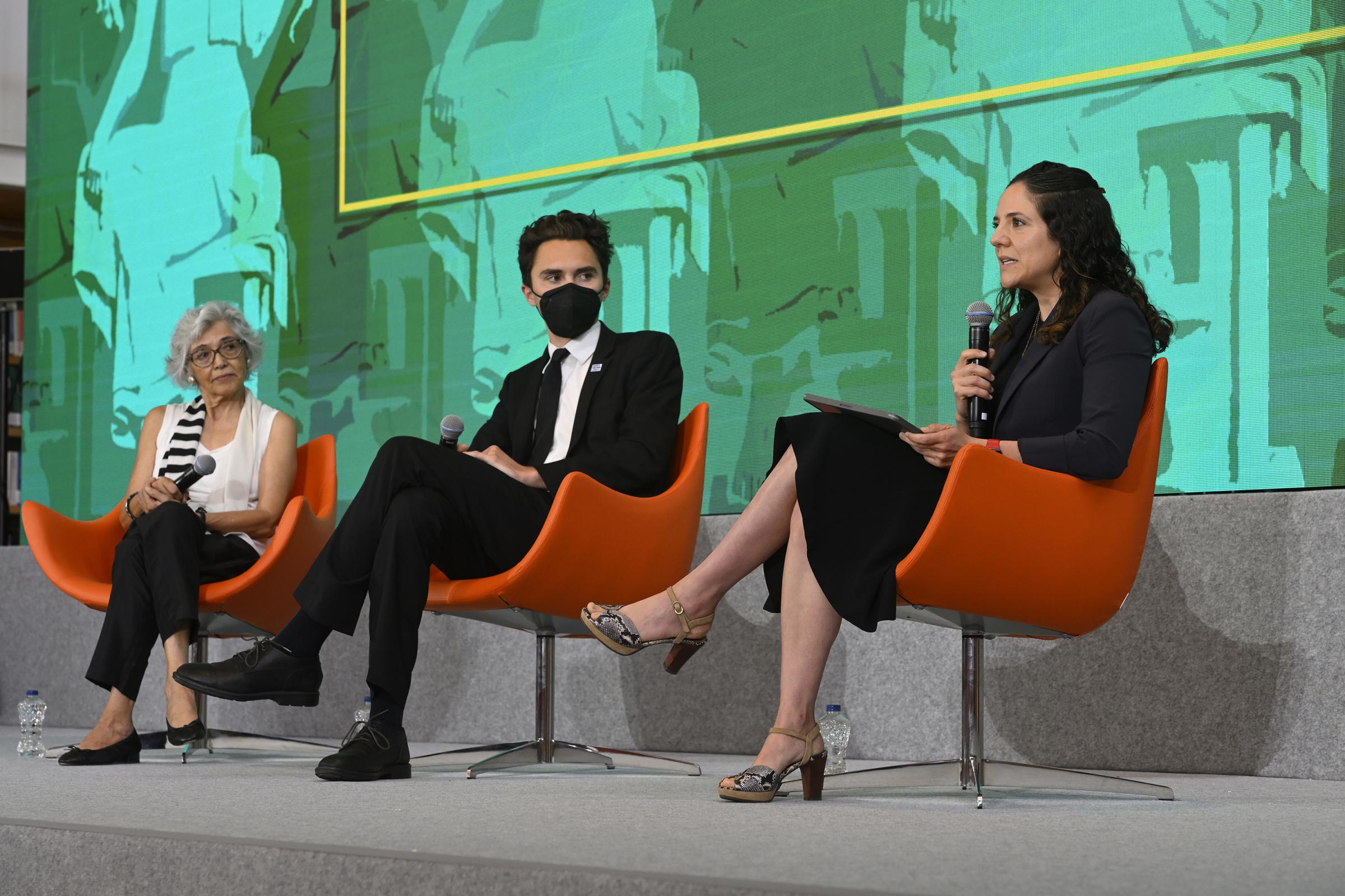 three panelists on stage in orange chairs