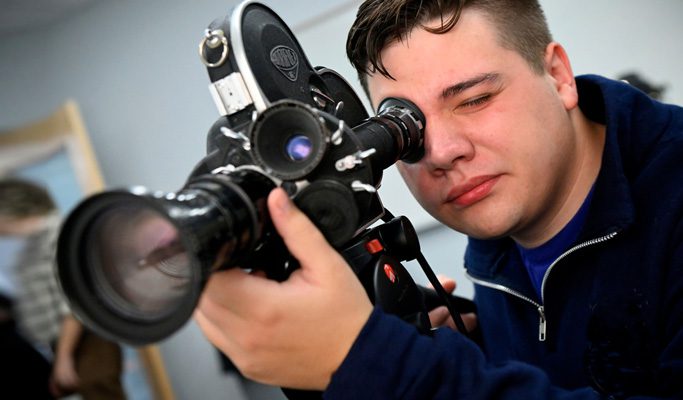 Undergraduate student looks through lens of camera for film and media studies class.