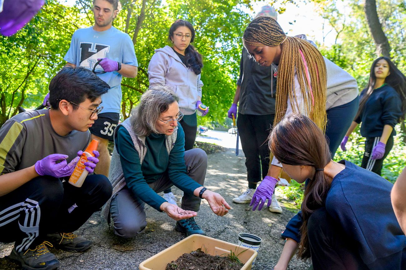 EPS professor Katalin Szlavecz looking at a soil sample with undergraduate students gathered around.