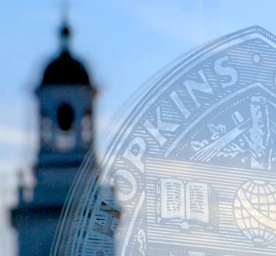 Gilman Hall tower reflected in glass door etched with JHU shield