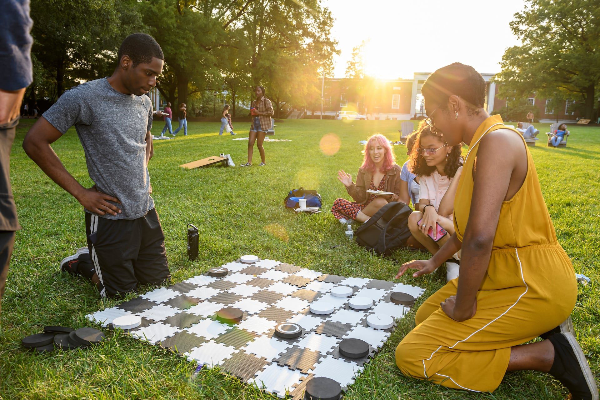 Students sitting on the quad, gathered around a large checkerboard playing a game of checkers