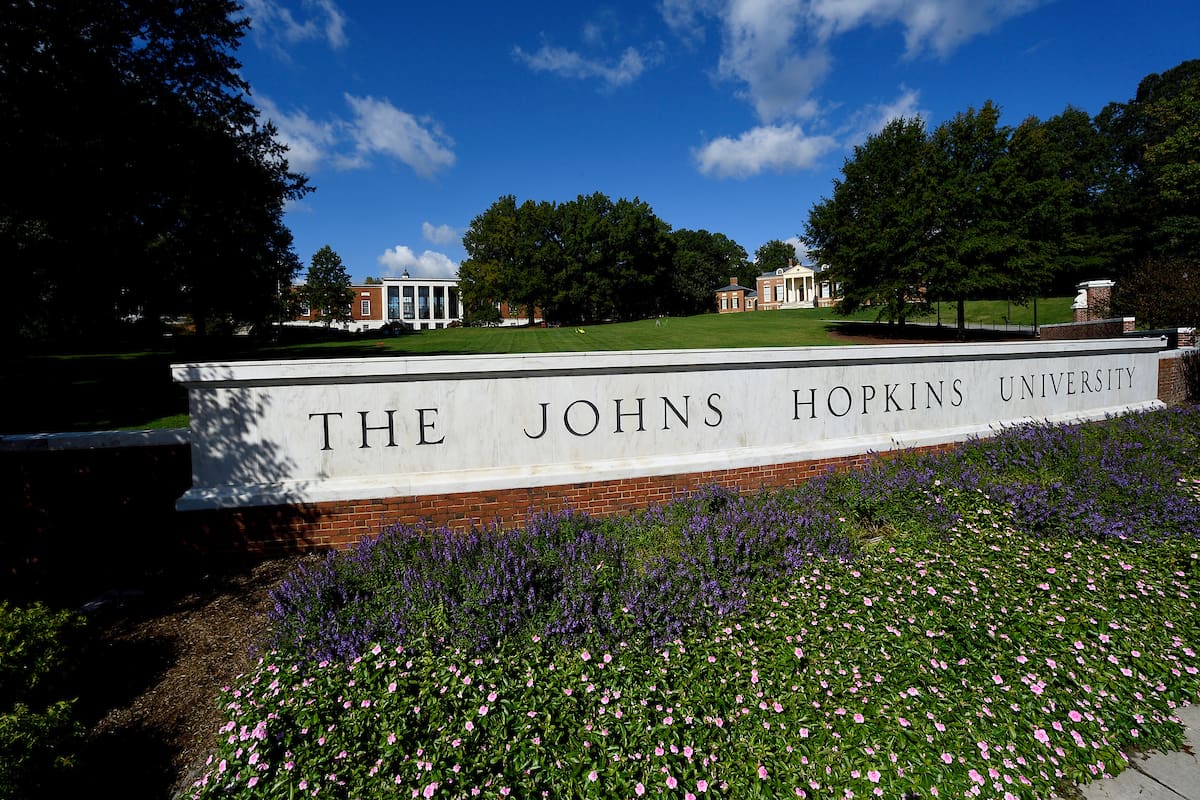 Johns Hopkins University wall in front of a green field with flowers