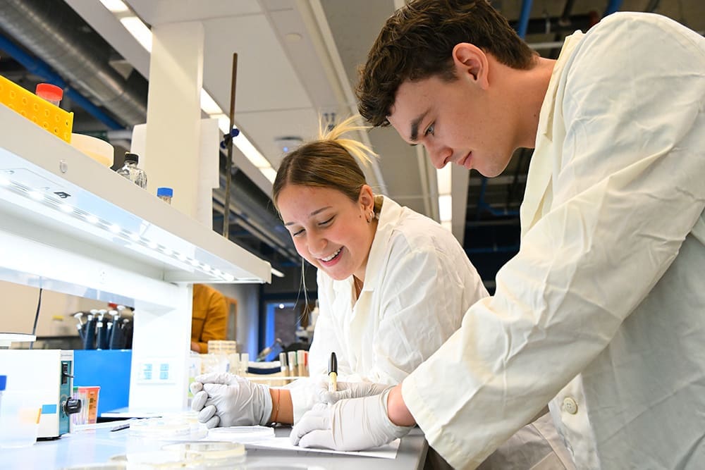 two students at biology lab bench making notes on their work