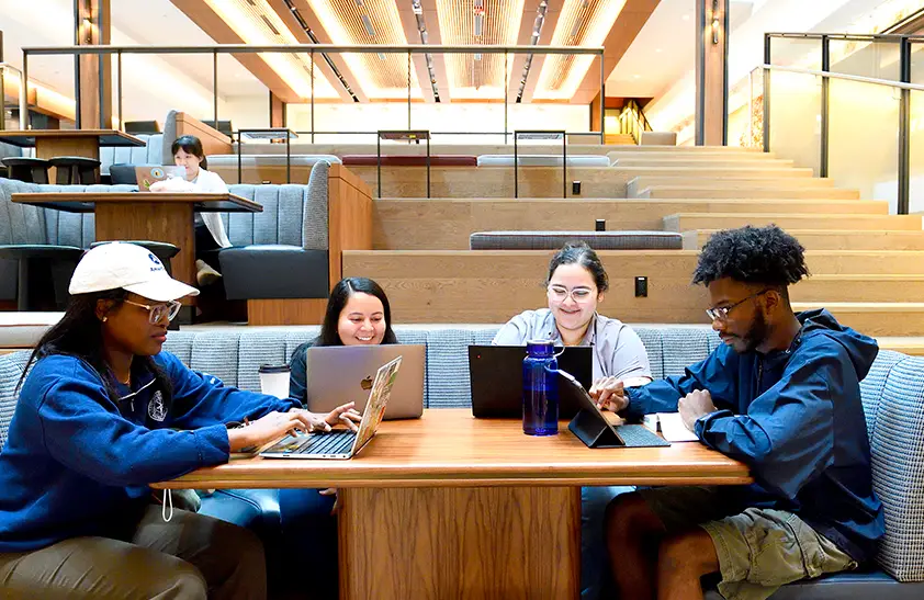 four students seated at booth working on their laptops