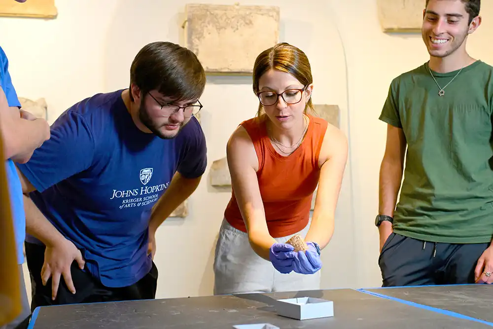 An instructor holds an artifact in the JHU Archaeological Museum as two students watch attentively.