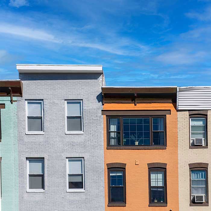 A row of colorful rowhouses under a bright blue sky in the Remington neighborhood near the Homewood campus.