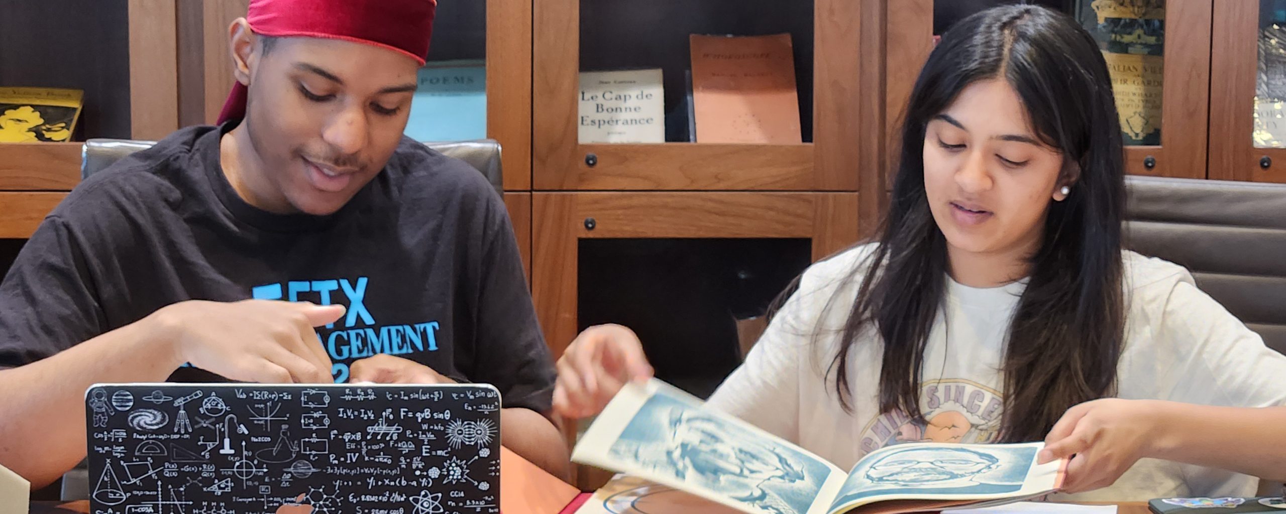 a student in a durag and a student with long black hair looking at books in a library room