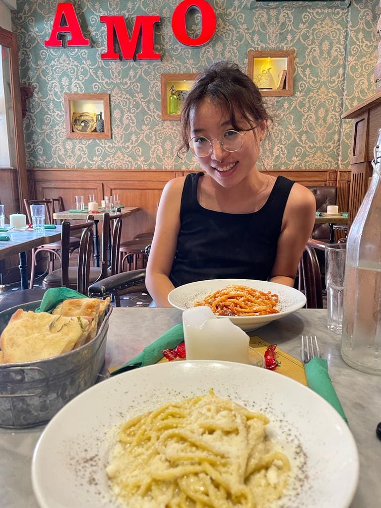 a student having pasta lunch at a restaurant in Trastevere. A bowl of noodles is in the foreground and the restaurant has Victorian wallpaper.