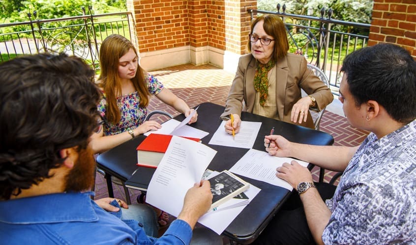 Professor Mary Jo Salter in discussion with several students outdoors at table on campus.